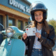 Jeune personne avec casque moto souriant tenant sa licence AM devant un scooter